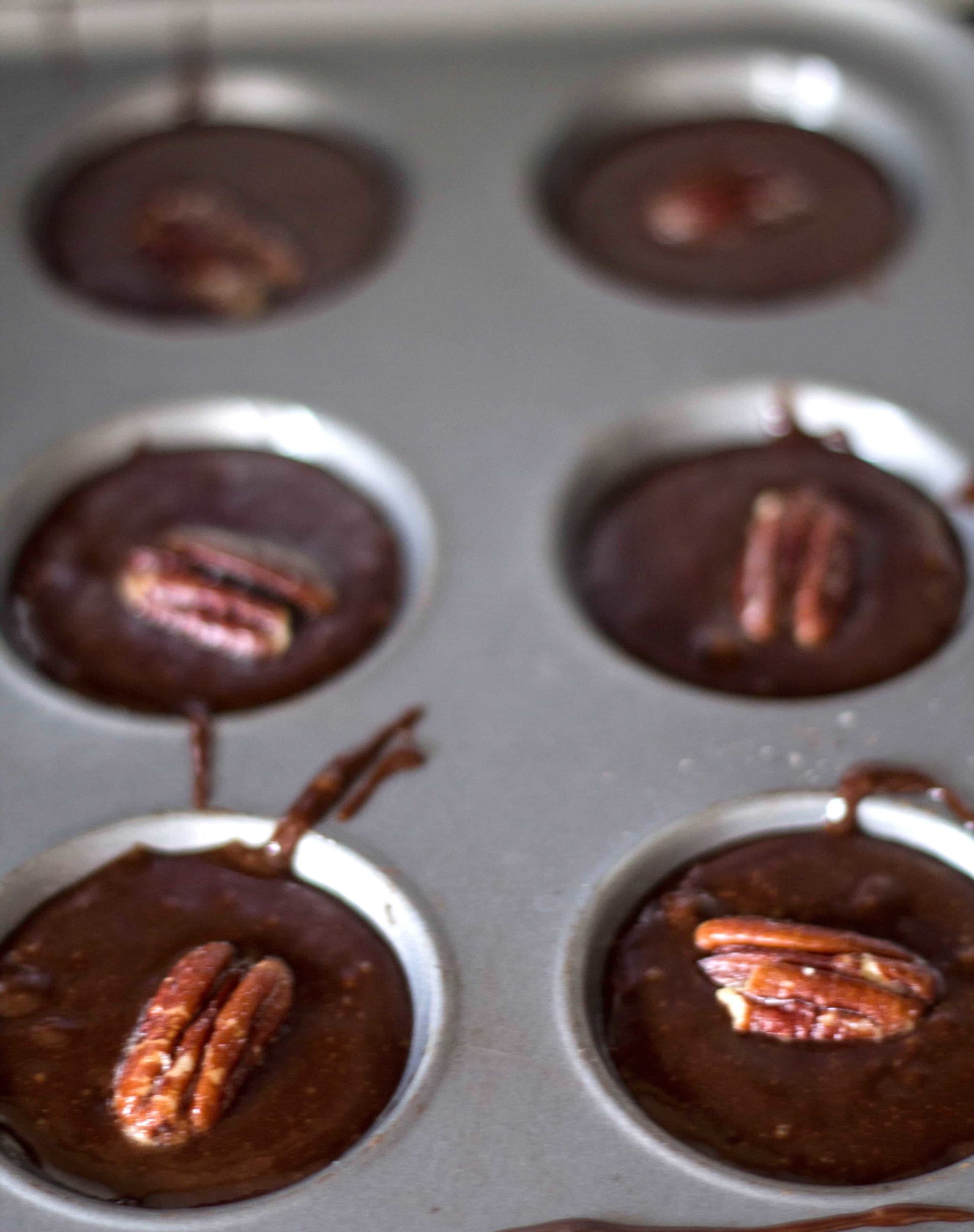 Triple Chocolate Mini Brownies batter in a cake pan with pecan nuts on top