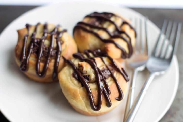 three chocolate swirl buns on a plate with two forks beside them.