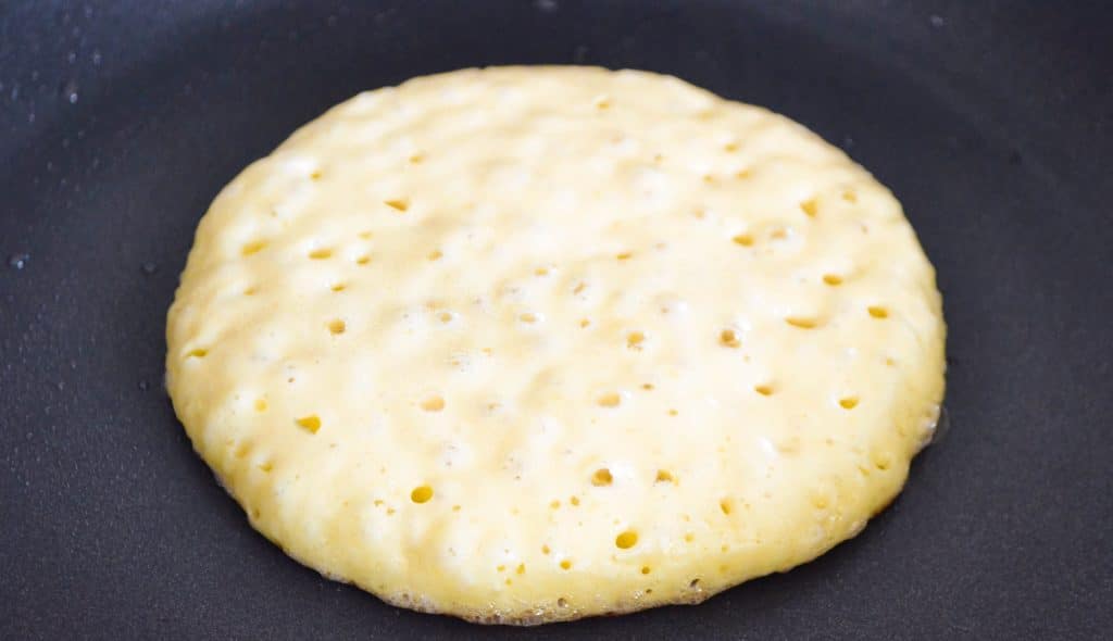 A pancake with bubbles cooking in a pan