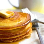 A Stack of bright yellow cornbread pancakes with a square of butter and syrup on top