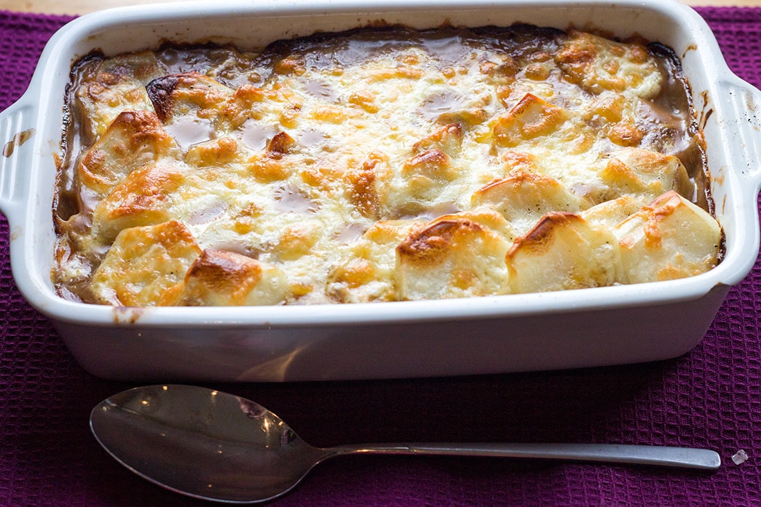 cottage pie topped with potato gratin in a serving dish with a spoon