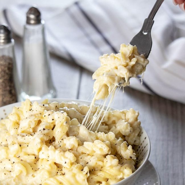 A fork digging into a big bowl of Homemade Creamy Mac and Cheese with cheese stretching from the dish