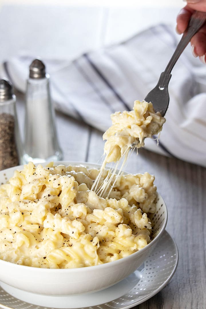 A fork digging into a big bowl of Homemade Creamy Mac and Cheese with cheese stretching from the dish