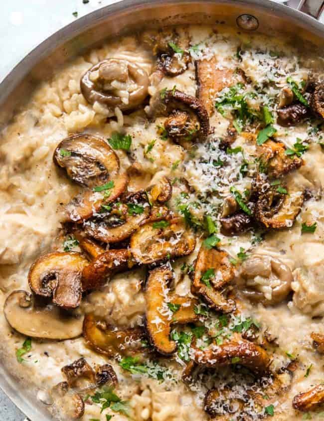 A close up image of a pan of chicken and mushroom risotto sprinkled with grated cheese and parsley.