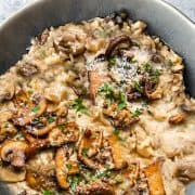 A close up image of a dish full of chicken and mushroom risotto sprinkled with grated cheese and parsley.
