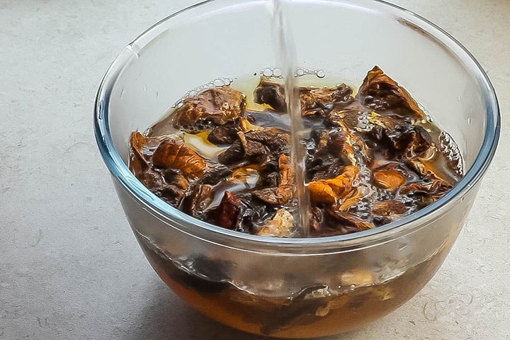 A glass bowl with hot water being poured onto dried mushrooms