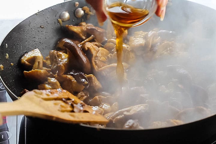 The rice wine being poured into the chicken and mushroom mixture in the wok.