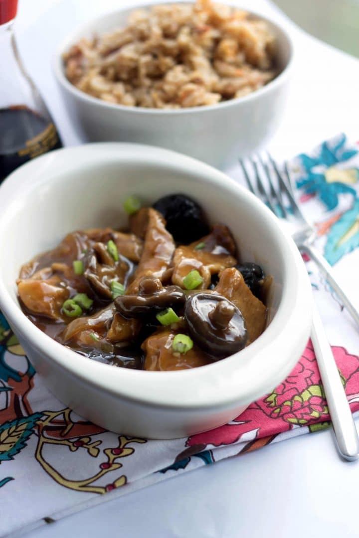 A dish of Chicken with Chinese mushrooms with fried rice in the background