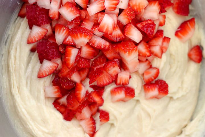 cake batter in a mixing bowl with chopped strawberries 