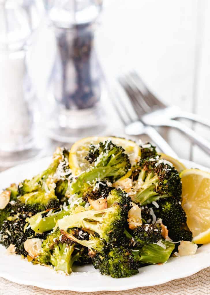 roasted broccoli piled high on a plate scattered with grated cheese and brown garlic