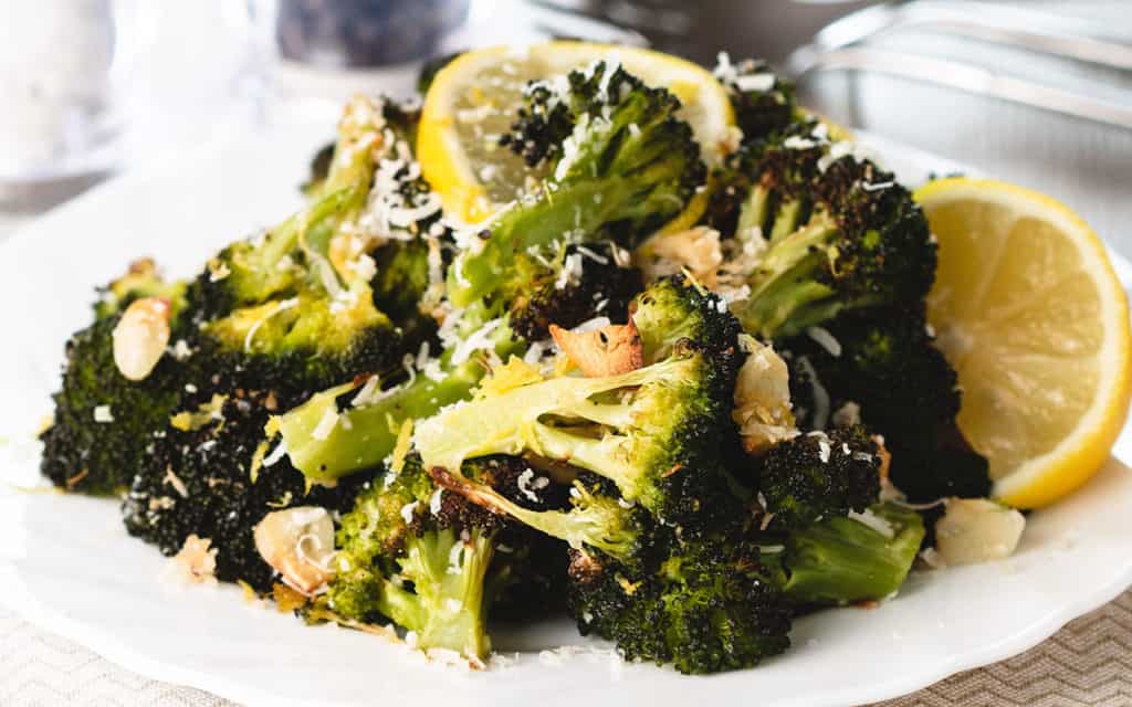 a close up of roasted broccoli piled high on a plate scattered with grated cheese and brown garlic