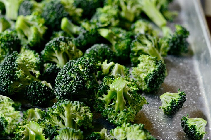 Broccoli florets coated in olive oil laid out onto a baking sheet.
