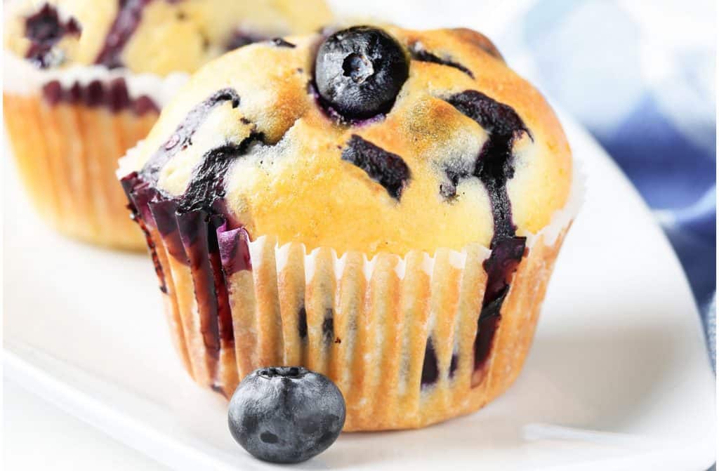 a blueberry muffin topped with a fresh blueberry with more muffins in the background