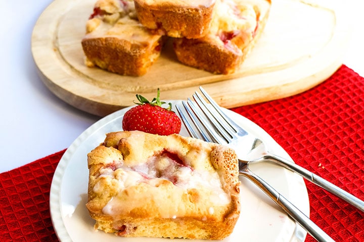 a strawberry cake on a plate with two forks beside it and more cakes in the background