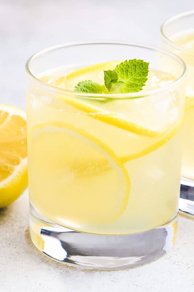 a glass of Homemade Hard Lemonade garnished with lemon slices and a sprig of mint