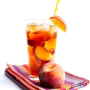 A glass of Sweet Peach Iced Tea with ice and a straw and a fresh wedge of peach on the glass