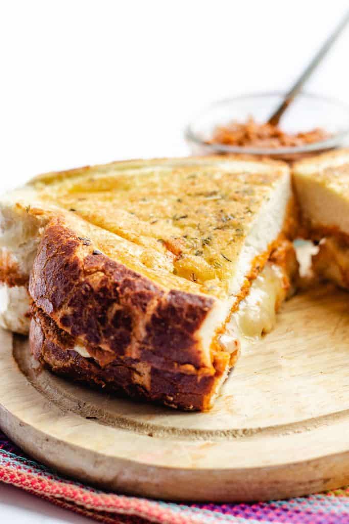 A golden grilled cheese sandwich on a cutting board with cheese oozing out of the middle