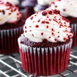 a Red Velvet Cupcakes with Cream Cheese Icing sprinkled with cake crumbs and more cupcake in the background