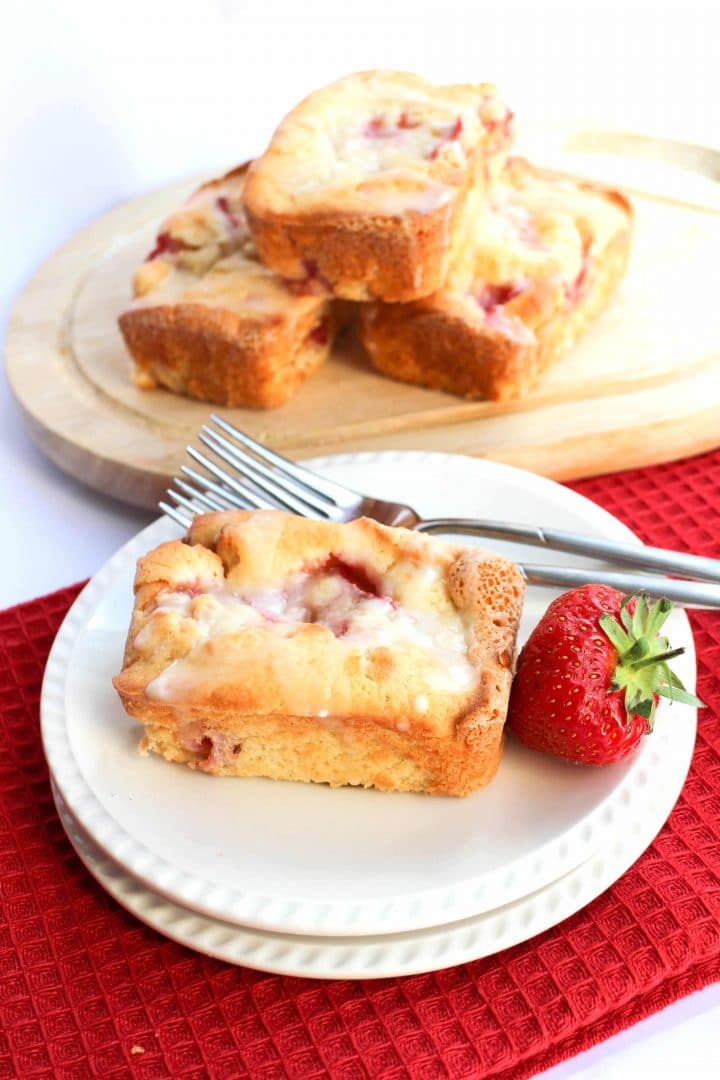 a strawberry cake on a plate with two forks beside it and more cakes in the background