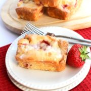 A strawberry cake on a plate with a fork and fresh strawberry next to it