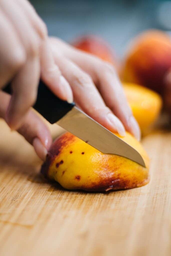 a peach being sliced on a cutting board.