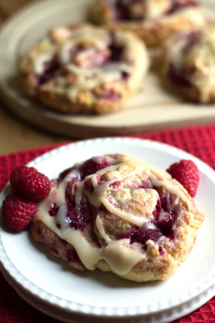 an Iced Raspberry Scone on a plate with fresh raspberries with more in the background.