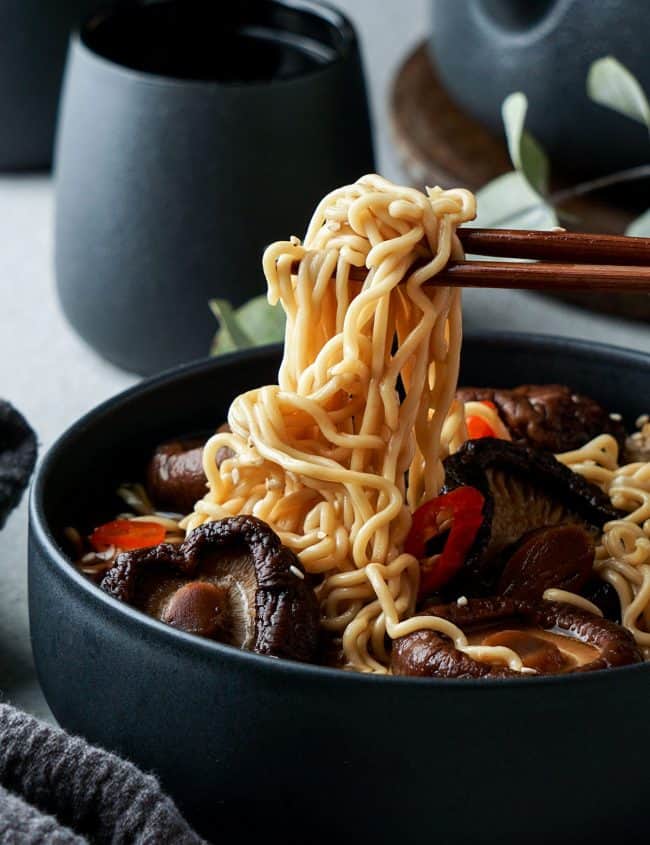 Chinese Mushroom Noodle Soup in a bowl with noodles on chopsticks.