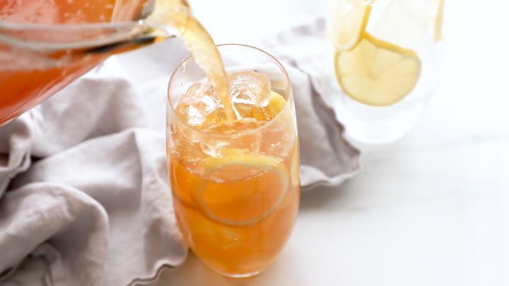 Sweet lemon iced tea being poured over lots of ice and lemon slices