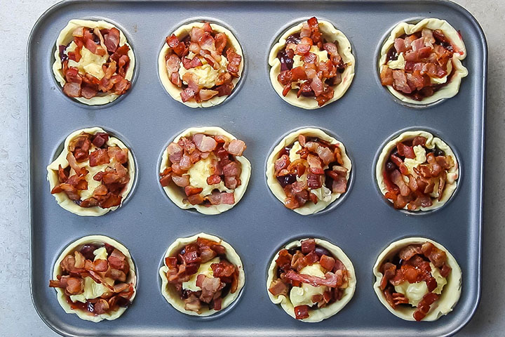 The cooked bacon scattered over the top of the filled tarts