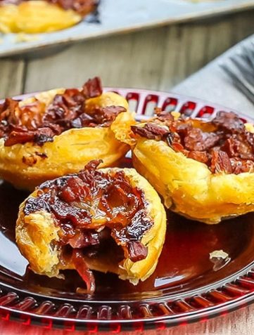 Three Cranberry Brie Tarts with Bacon & Red Onion on a red plate with more tarts in the background
