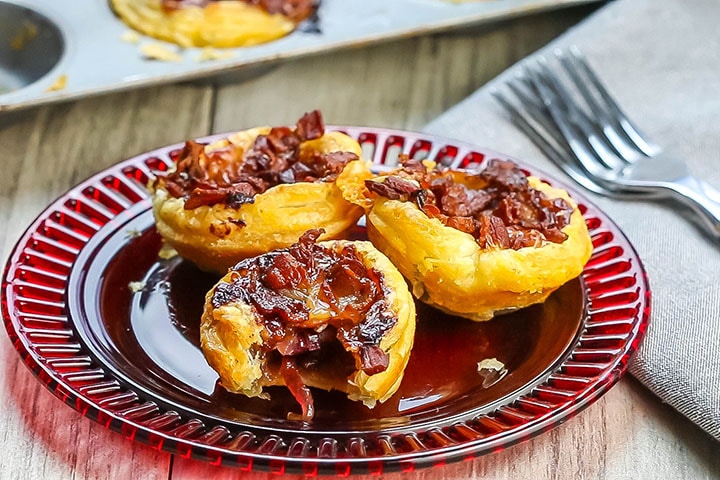 Three Cranberry Brie Tarts on a red plate with more tarts in the background