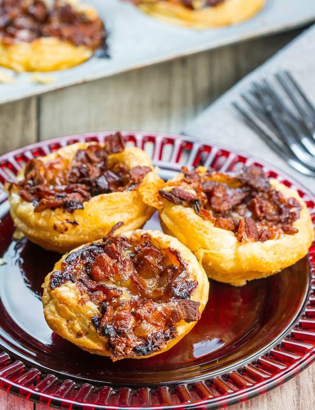 Three Cranberry Brie Tarts with Bacon & Red Onion on a red plate with more tarts in the background