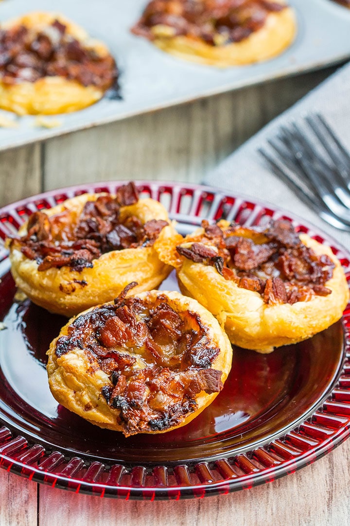 Three Cranberry Brie Tarts on a red plate with more tarts in the background