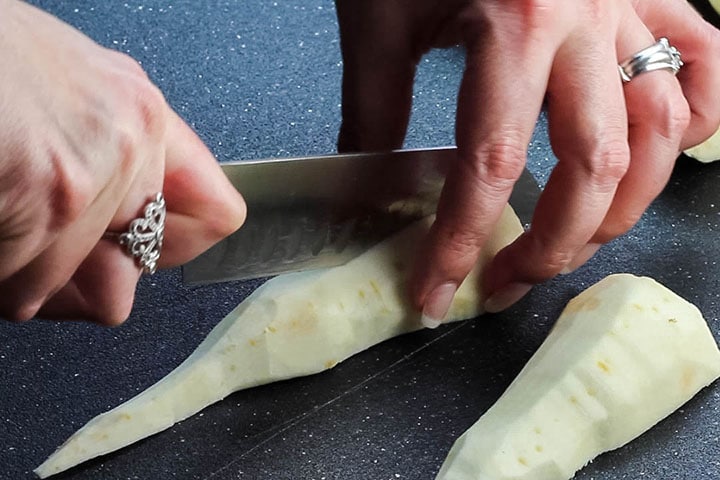 A parsnip being sliced on a cutting board