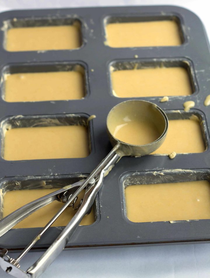 A mini loaf pan filled with the batter with a ice cream scoop laying across the pan