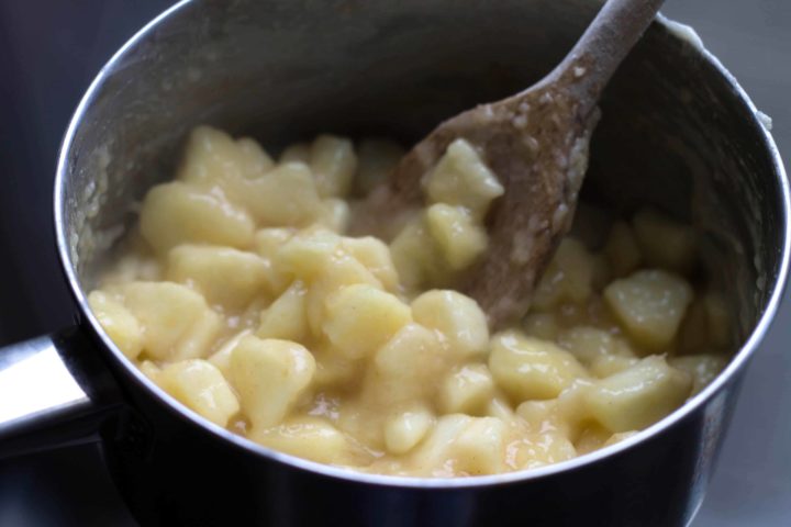 chopped apple in a pan being stirred with a wooden spoon