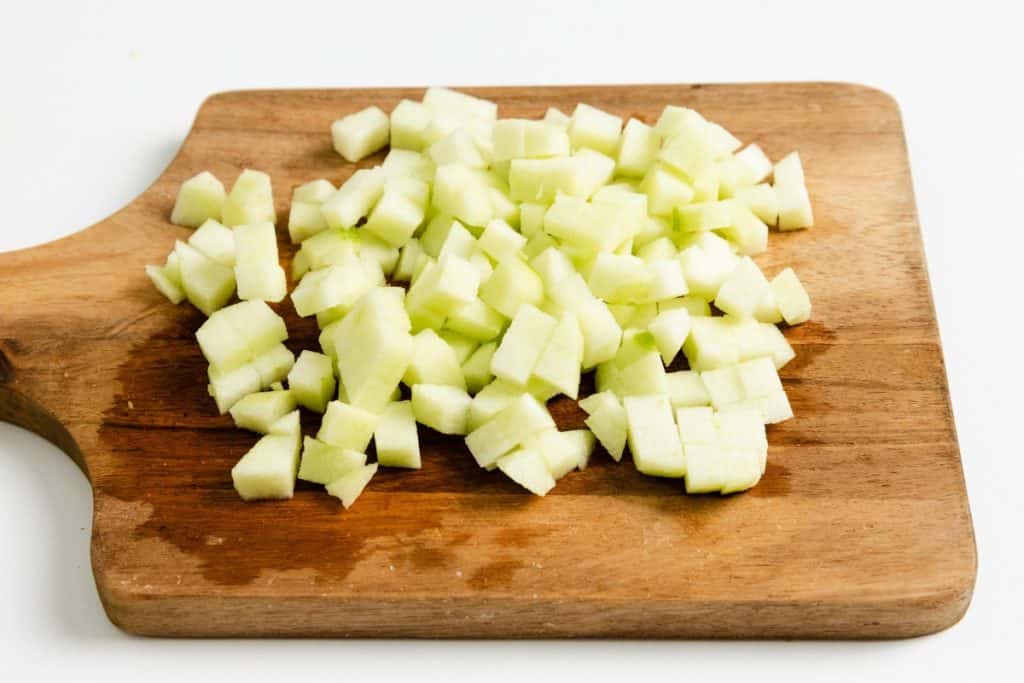 Diced green apple pieces on a wooden cutting board with a white background, perfect for topping Apple Cheesecake Muffins.