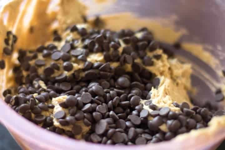 chocolate chips being added to the cookie dough in a plastic bowl.