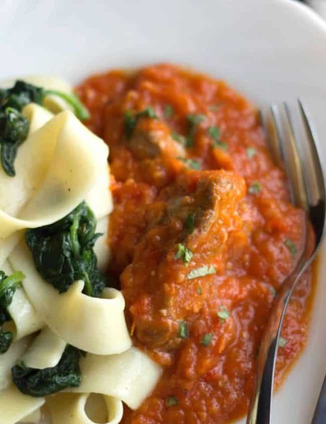 A close up of a plate of Sicilian lamb with pasta and a fork
