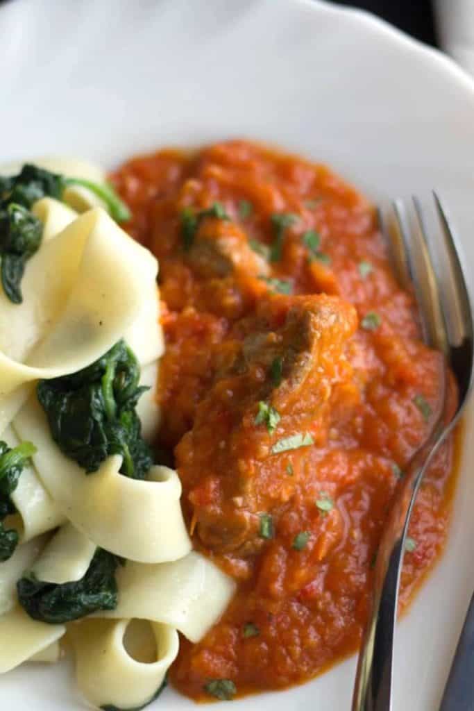 A close up of a plate of Sicilian lamb with pasta and a fork