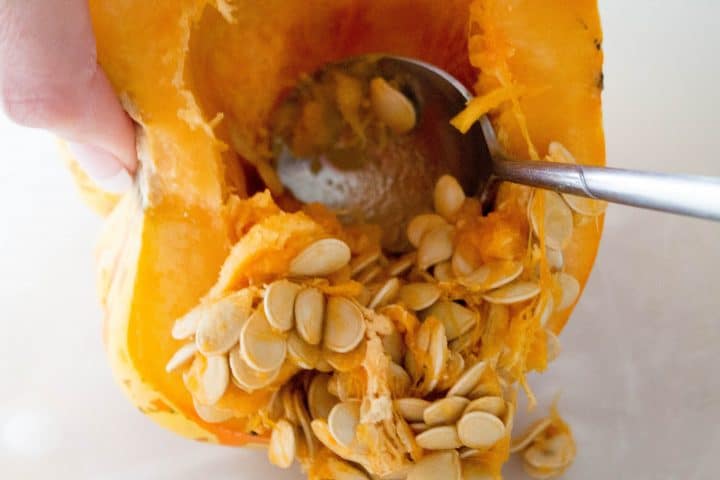 A spoon removing the seeds from the middle of the squash 