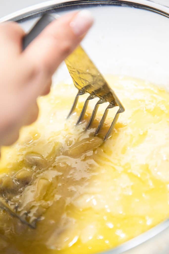 the bananas being mashed with the butter mixture in a bowl
