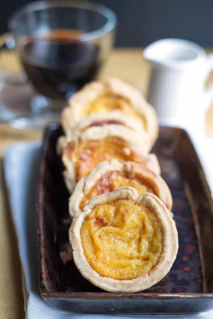 Custard Tarts lined on a pplate with a cup of coffee in the background