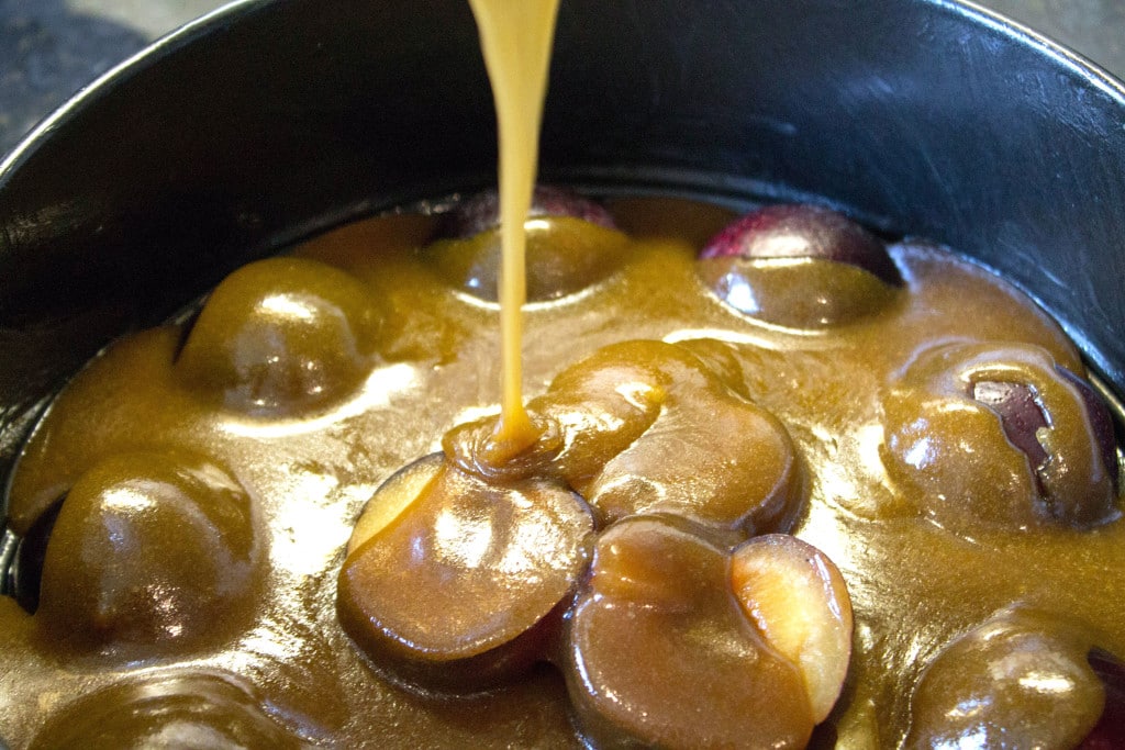 plums sliced in half in a pan with caramel being poured on them