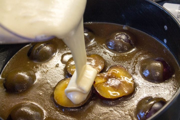 batter being poured over the butter and plums in a baking tin