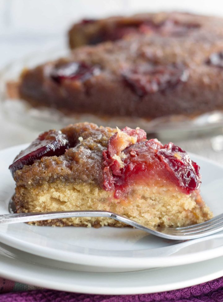 side view of a pice of plum upside down cake on a plate with a fork next to it