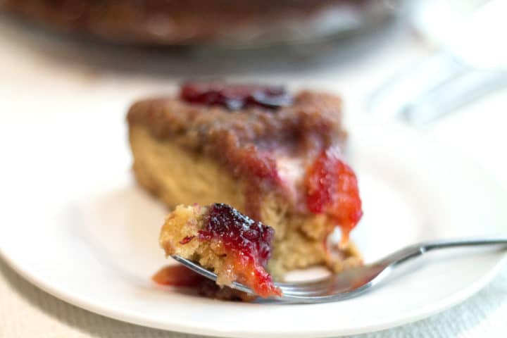 a front view of a piece of plum upside down cake on a plate with a piece of the cake on a fork next to it