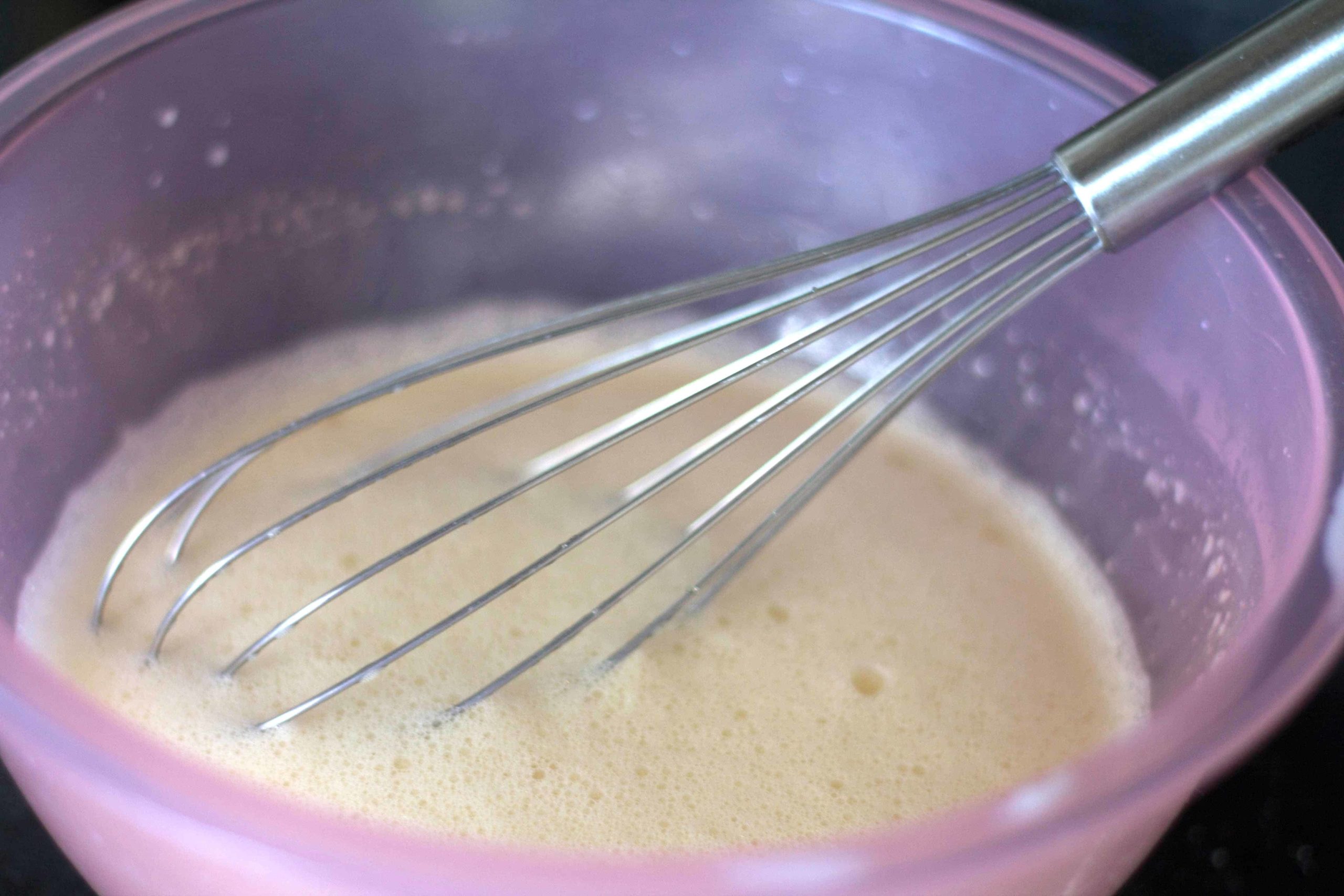 milk and egg mixture being whisked in a pink bowl