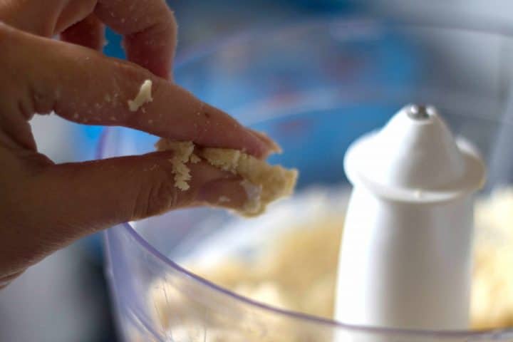 fingers pinching the mixture to test the structure, with the food mixer in the background
