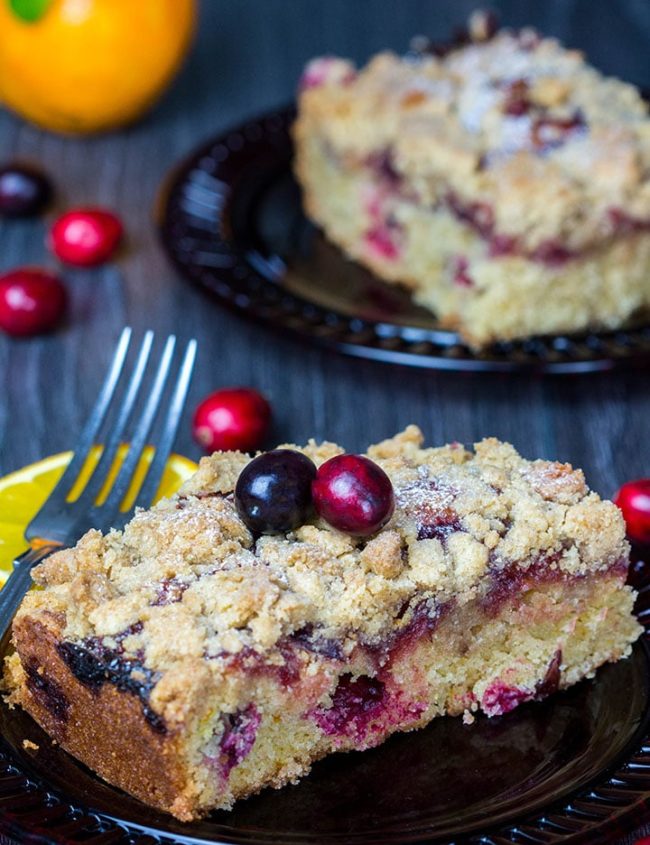 A piece of Cranberry Orange Crumb Cake with cranberries scattered around it in the table